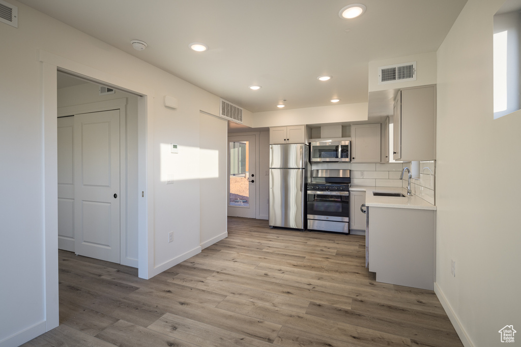 Kitchen with appliances with stainless steel finishes, a sink, light wood finished floors, baseboards, and recessed lighting