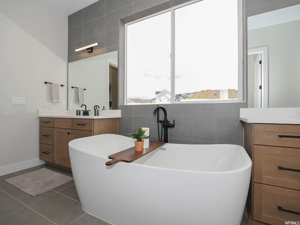 Bathroom with a bathing tub, mirror, tile flooring, vanity, and tile walls