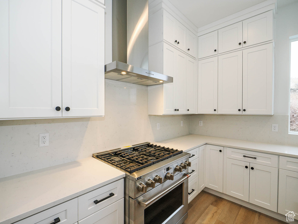 Kitchen with white cabinets, light hardwood / wood-style floors, wall chimney range hood, and stainless steel range