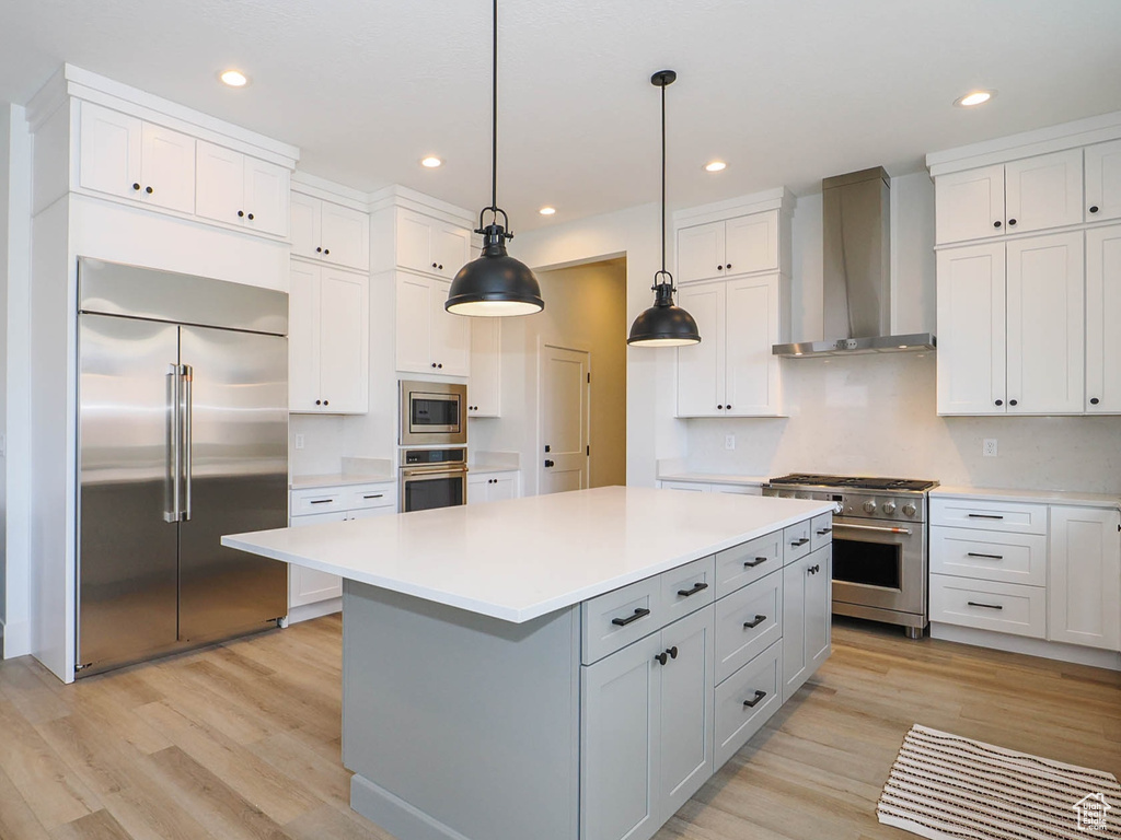 Kitchen featuring wall chimney exhaust hood, built in appliances, a kitchen island, and light wood-type flooring