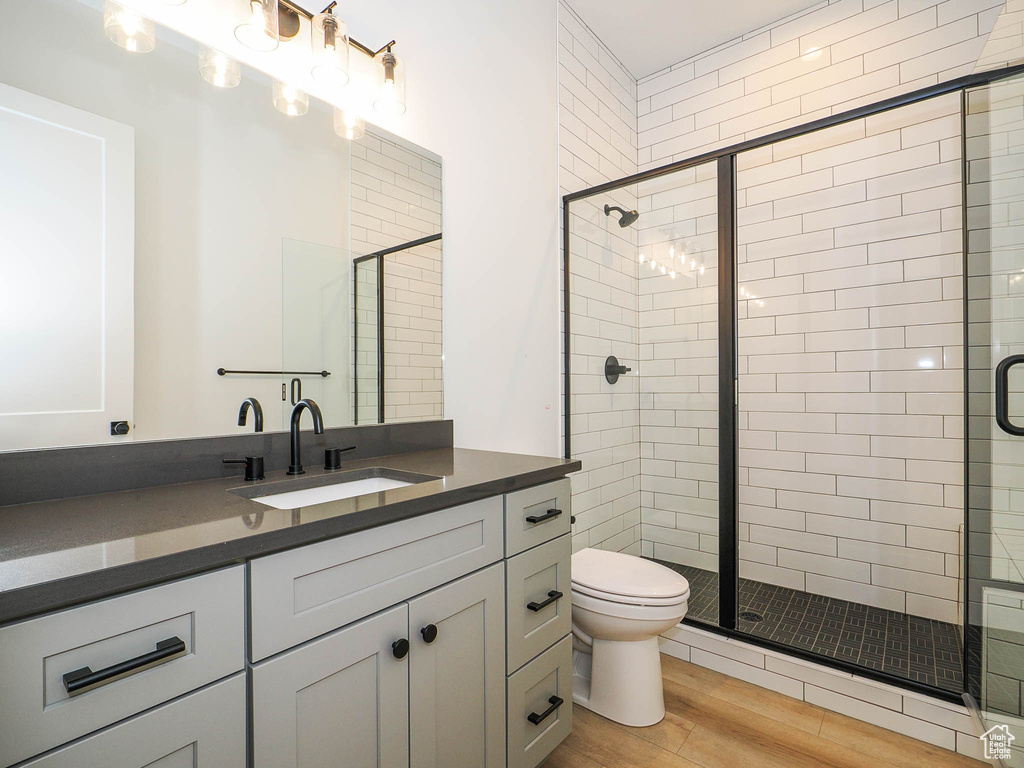 Bathroom featuring hardwood / wood-style floors, toilet, vanity with extensive cabinet space, and a shower with door