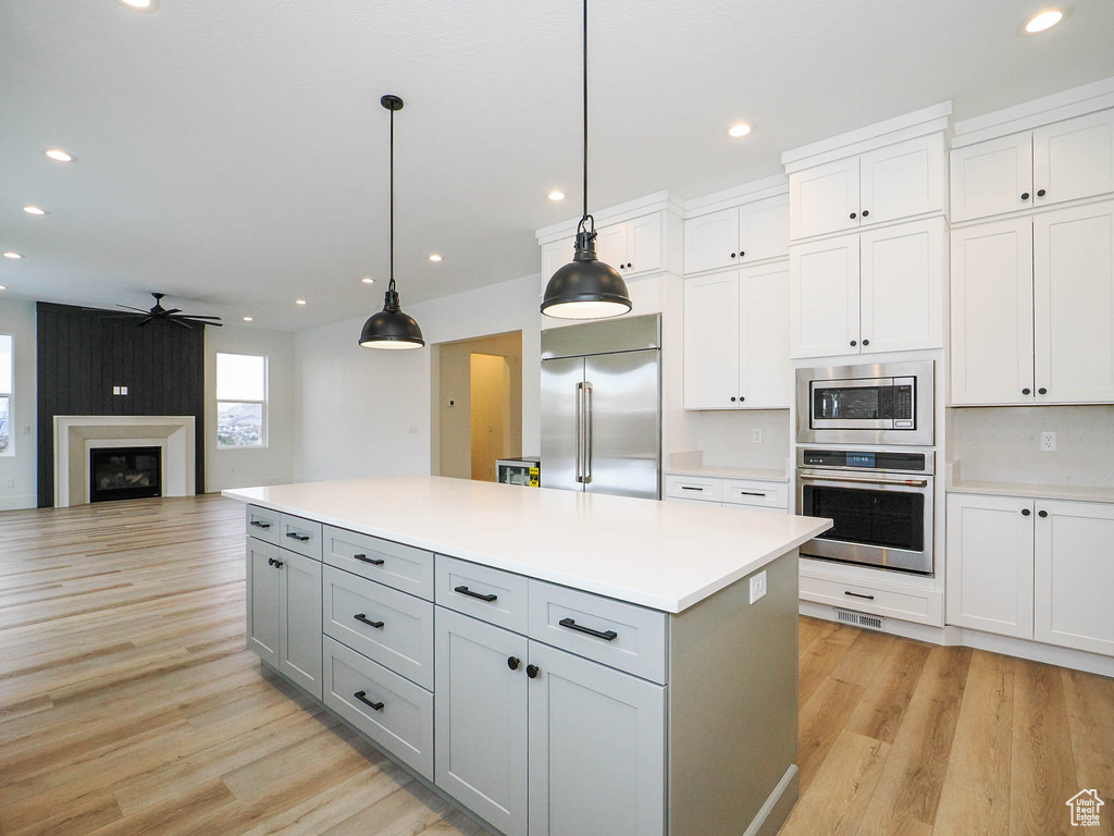 Kitchen featuring built in appliances, hanging light fixtures, white cabinets, light hardwood / wood-style flooring, and ceiling fan