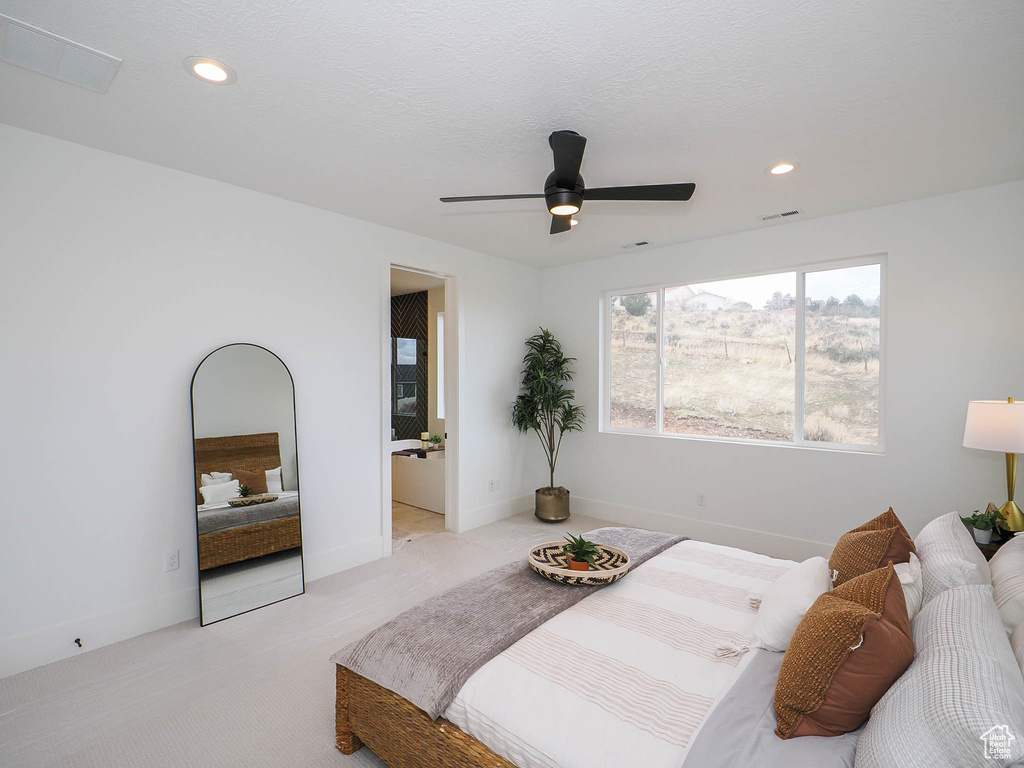 Bedroom with light colored carpet, ensuite bathroom, and ceiling fan