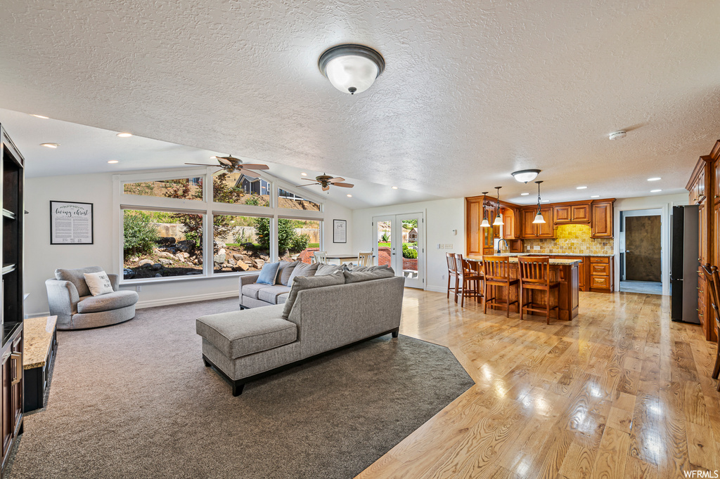 Carpeted living room with ceiling fan, a textured ceiling, a healthy amount of sunlight, and vaulted ceiling