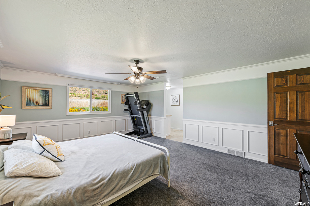Carpeted bedroom featuring ceiling fan, ornamental molding, and a textured ceiling