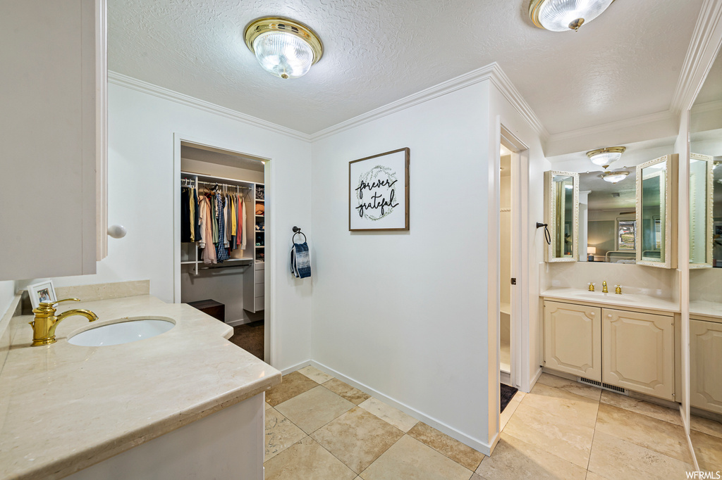 Bathroom featuring double large vanity, light tile floors, crown molding, a textured ceiling, and mirror