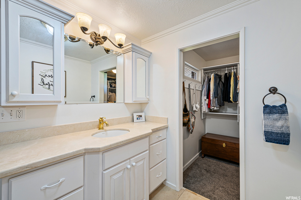 Bathroom featuring tile flooring, vanity with extensive cabinet space, a textured ceiling, mirror, and ornamental molding