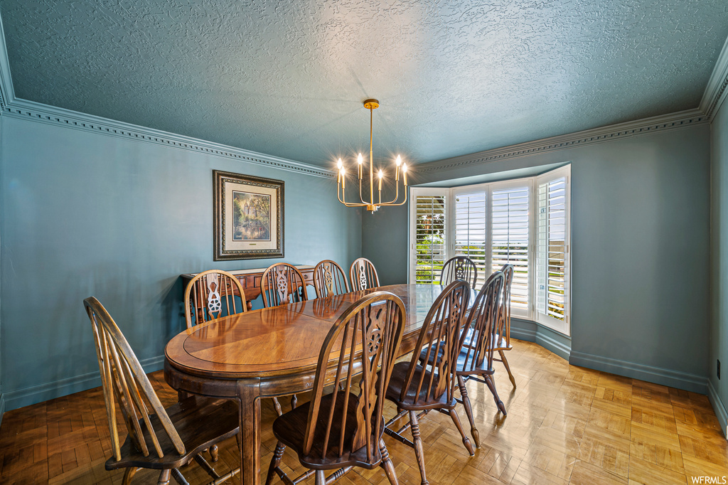 Dining area with crown molding, a textured ceiling, and light parquet flooring