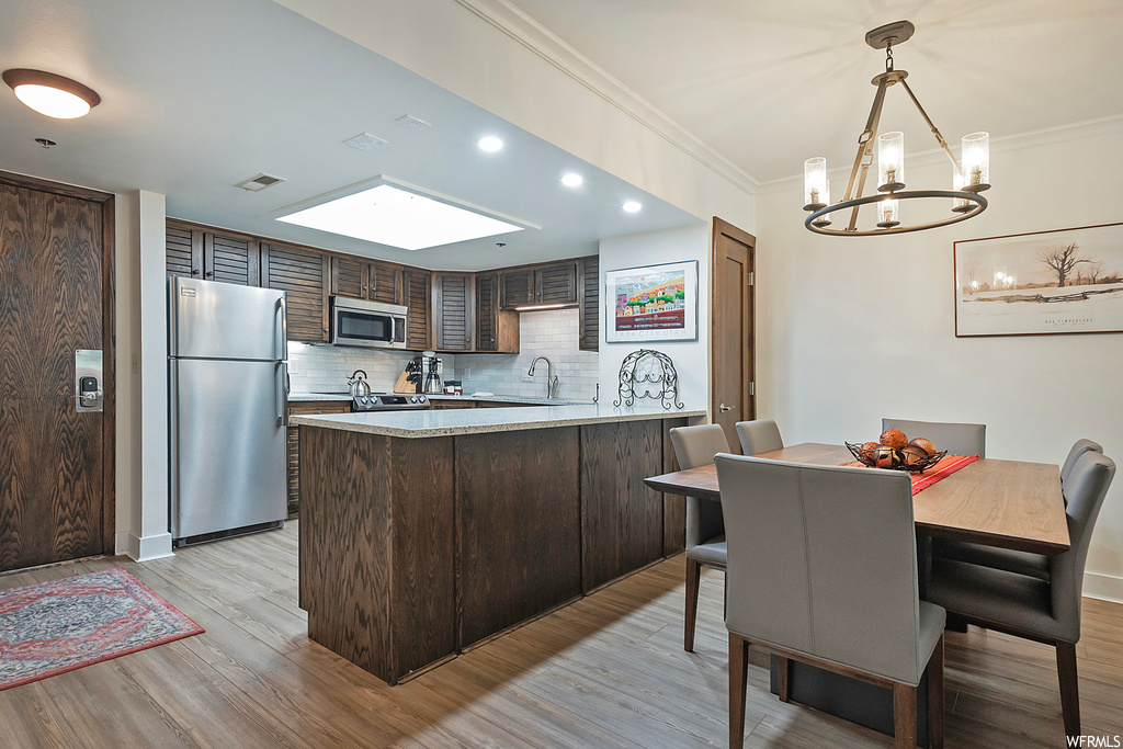 Kitchen featuring appliances with stainless steel finishes, a skylight, light countertops, backsplash, ornamental molding, and light hardwood floors