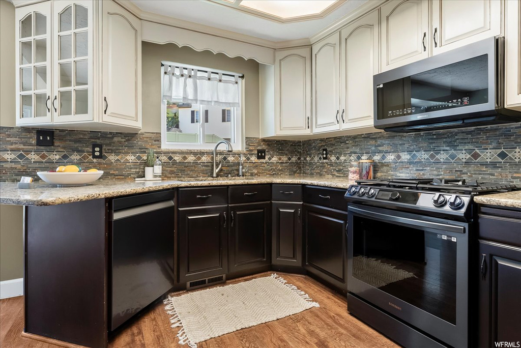 Kitchen with stone counters, black appliances, backsplash, hardwood floors, and ornamental molding