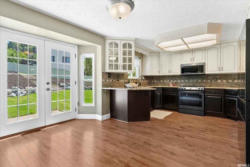 Kitchen featuring stainless steel appliances, a wealth of natural light, light hardwood flooring, backsplash, a textured ceiling, and white cabinetry