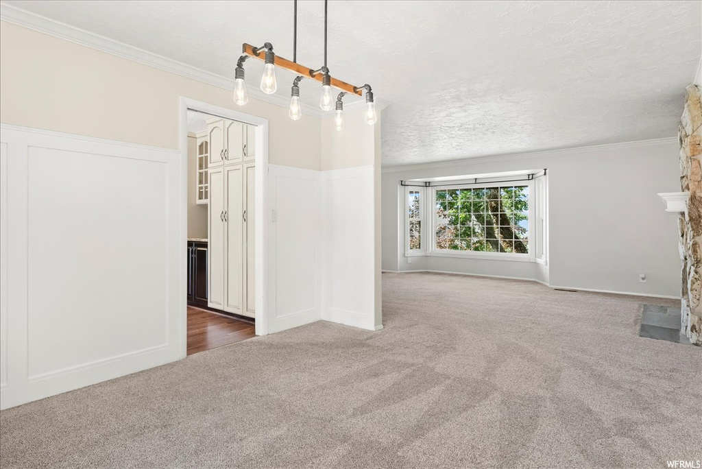 Spare room featuring light carpet, ornamental molding, and a textured ceiling