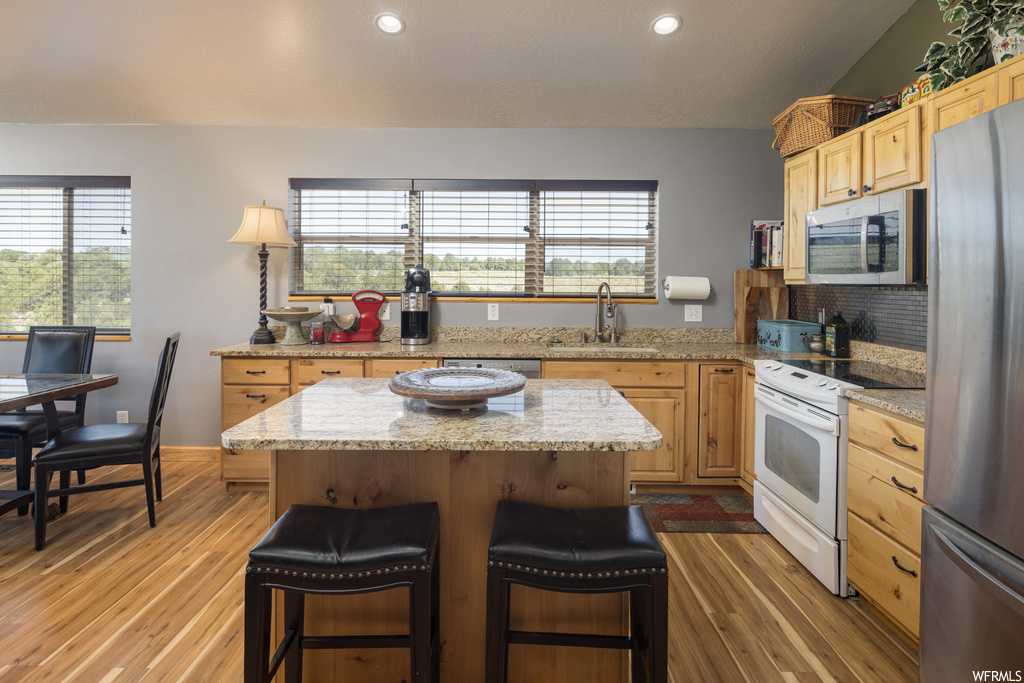 Kitchen featuring granite-like countertops, brown cabinets, a center island, light hardwood floors, and appliances with stainless steel finishes