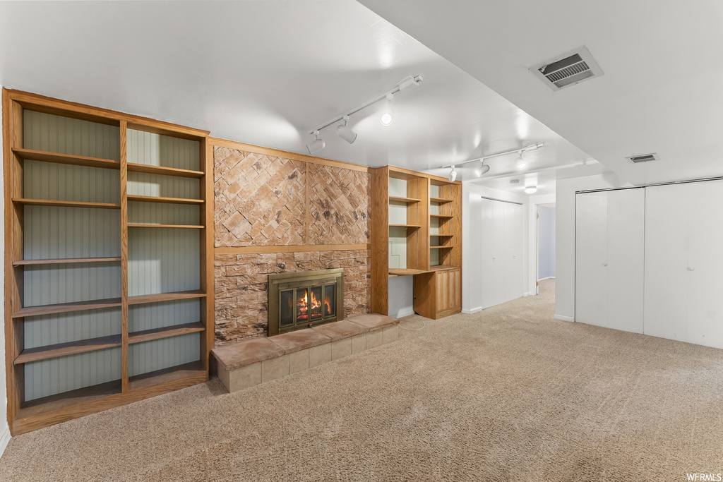 Unfurnished living room with rail lighting, a stone fireplace, and light carpet