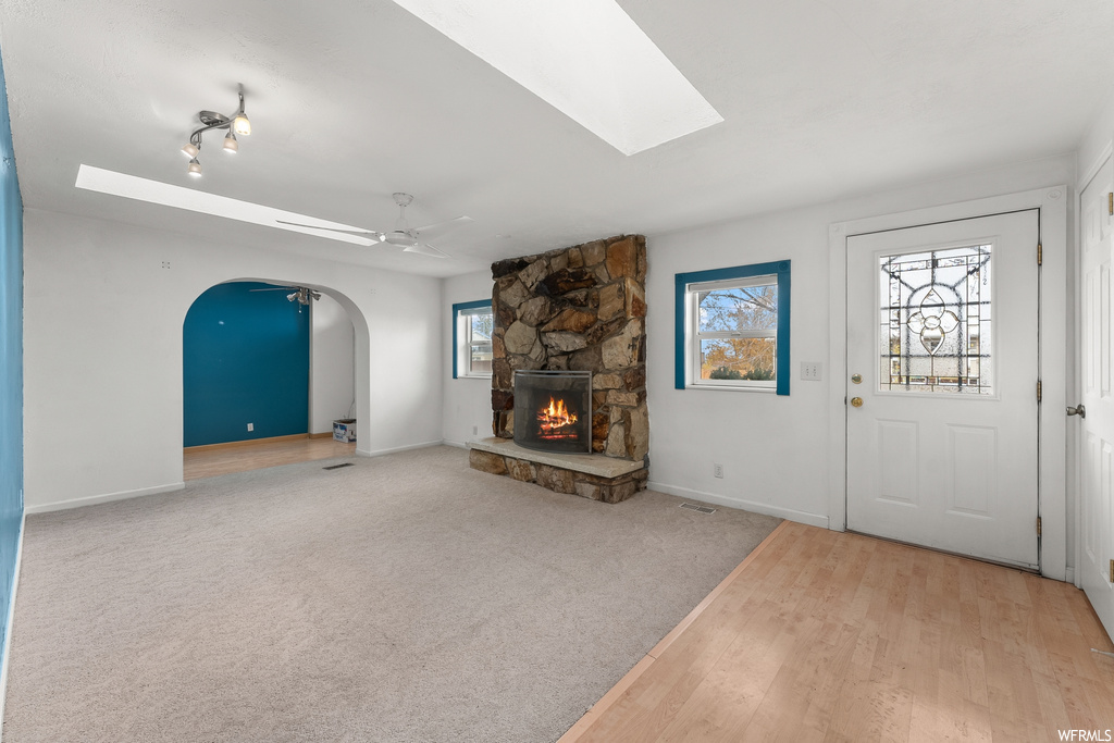 Foyer with light colored carpet, a stone fireplace, ceiling fan, a healthy amount of sunlight, and a skylight