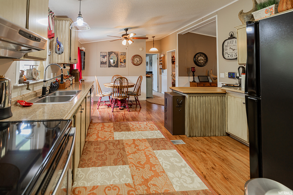 Kitchen with range hood, light hardwood flooring, ceiling fan, black refrigerator, pendant lighting, and light countertops