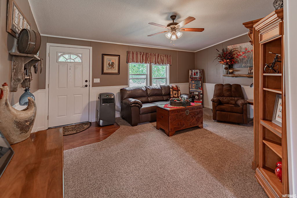 Living room with a textured ceiling, ceiling fan, crown molding, and carpet flooring
