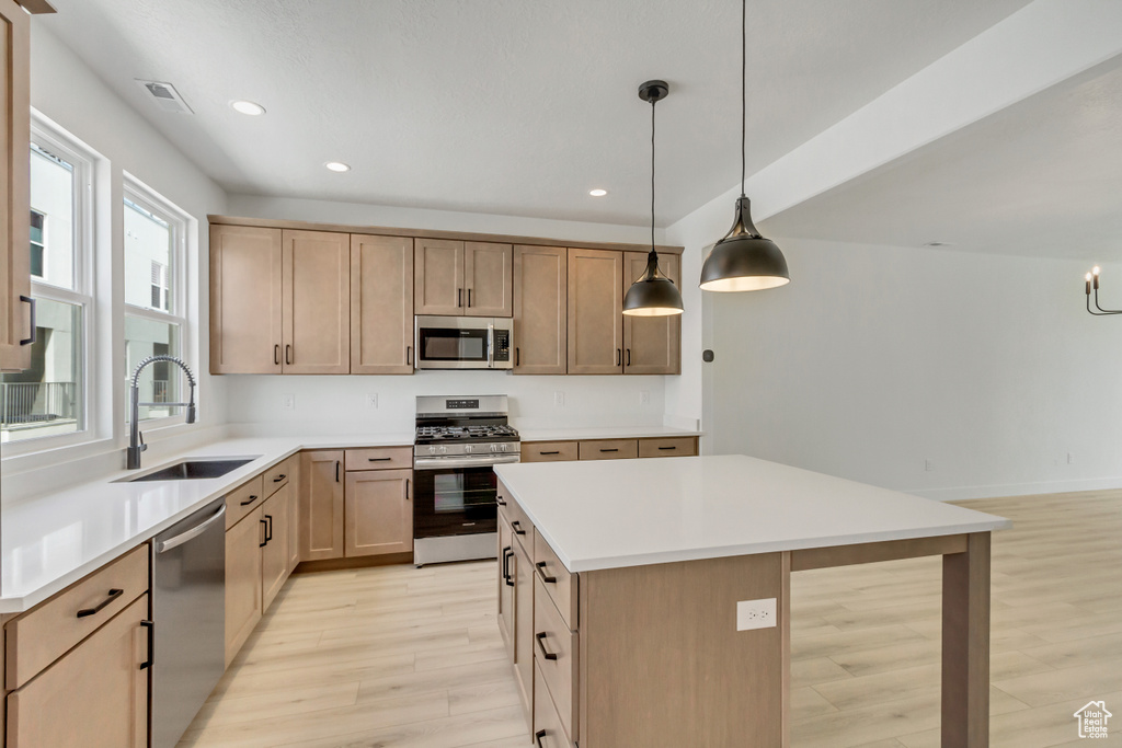 Kitchen featuring appliances with stainless steel finishes, light hardwood / wood-style floors, sink, pendant lighting, and a center island