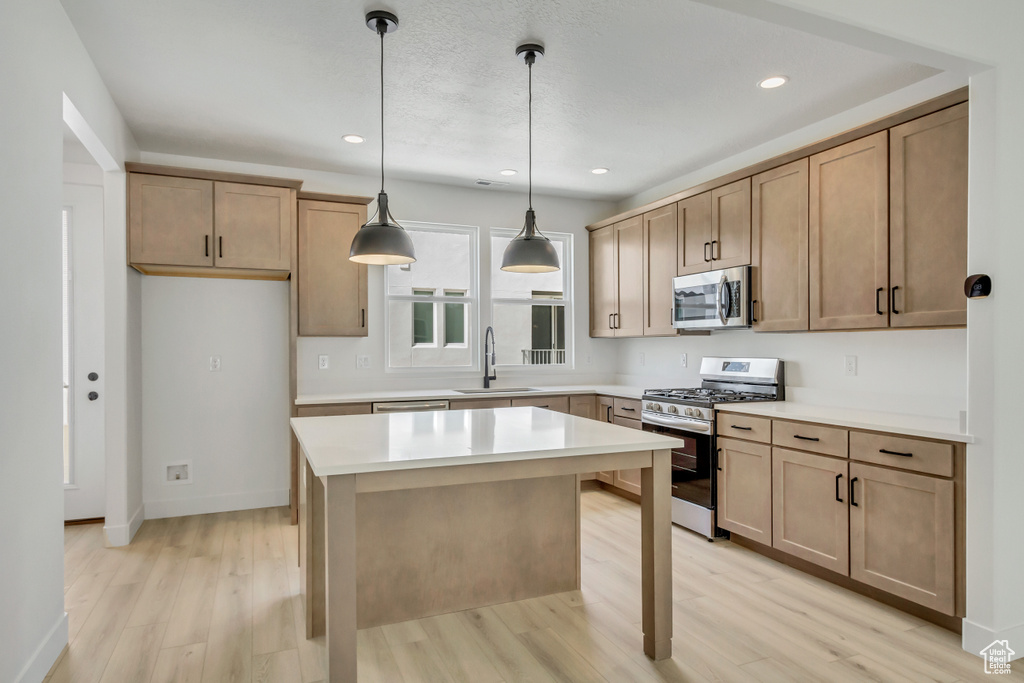 Kitchen featuring a center island, pendant lighting, light wood-type flooring, appliances with stainless steel finishes, and sink