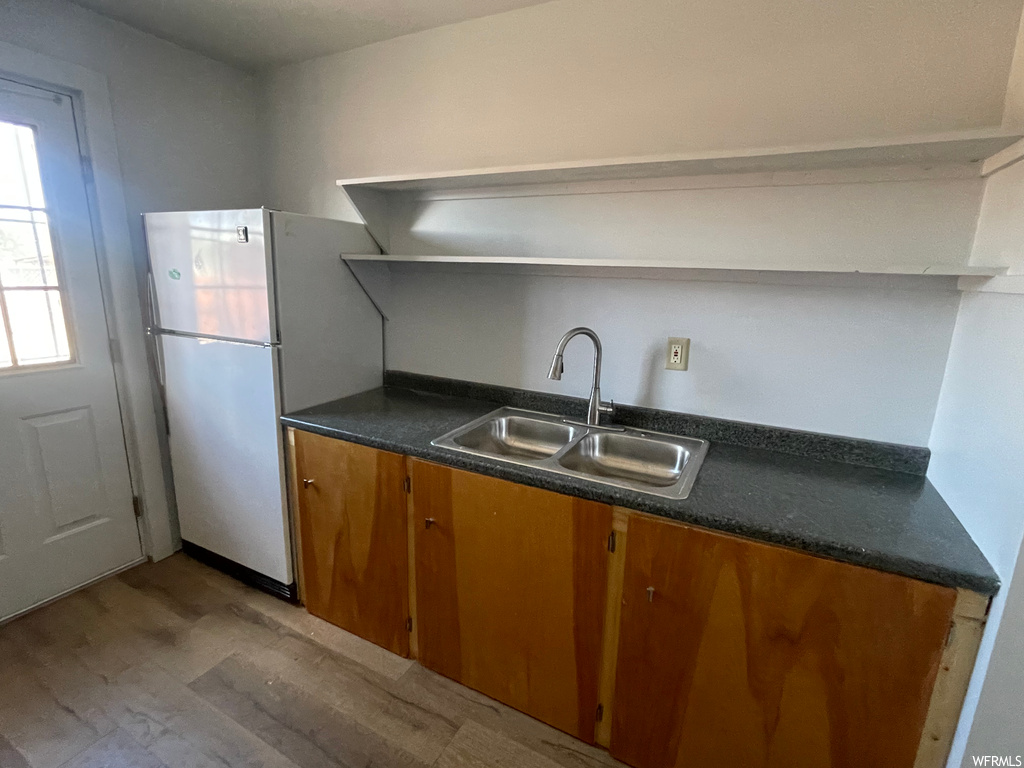 Kitchen featuring brown cabinets, fridge, dark countertops, and wood-type flooring