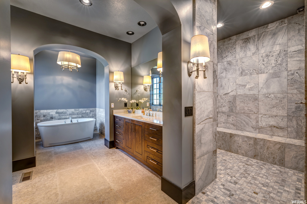 Bathroom with light tile floors, tile walls, vanity, mirror, and a bath
