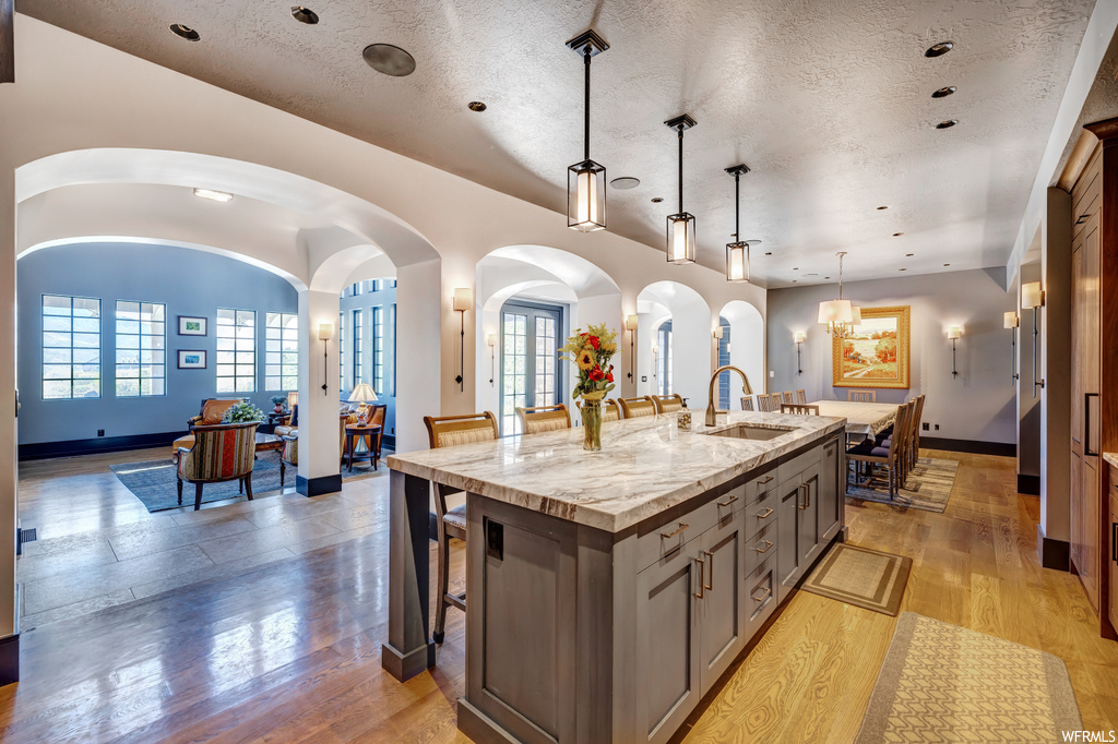Kitchen with decorative light fixtures, kitchen island with sink, light parquet floors, and a textured ceiling