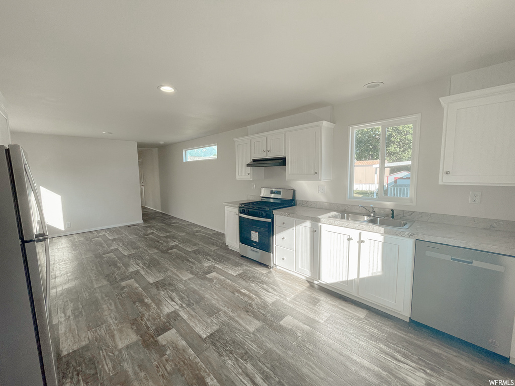 Kitchen featuring stainless steel appliances, white cabinetry, light countertops, and light hardwood flooring