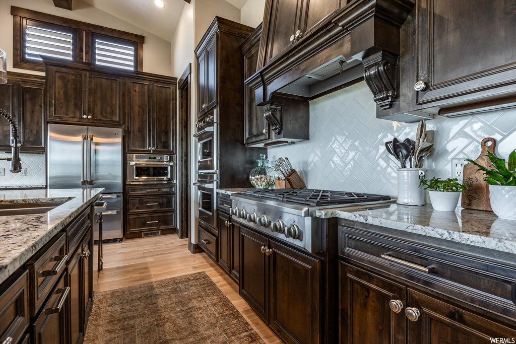 Kitchen featuring granite-like countertops, dark brown cabinets, backsplash, hardwood floors, lofted ceiling, and appliances with stainless steel finishes