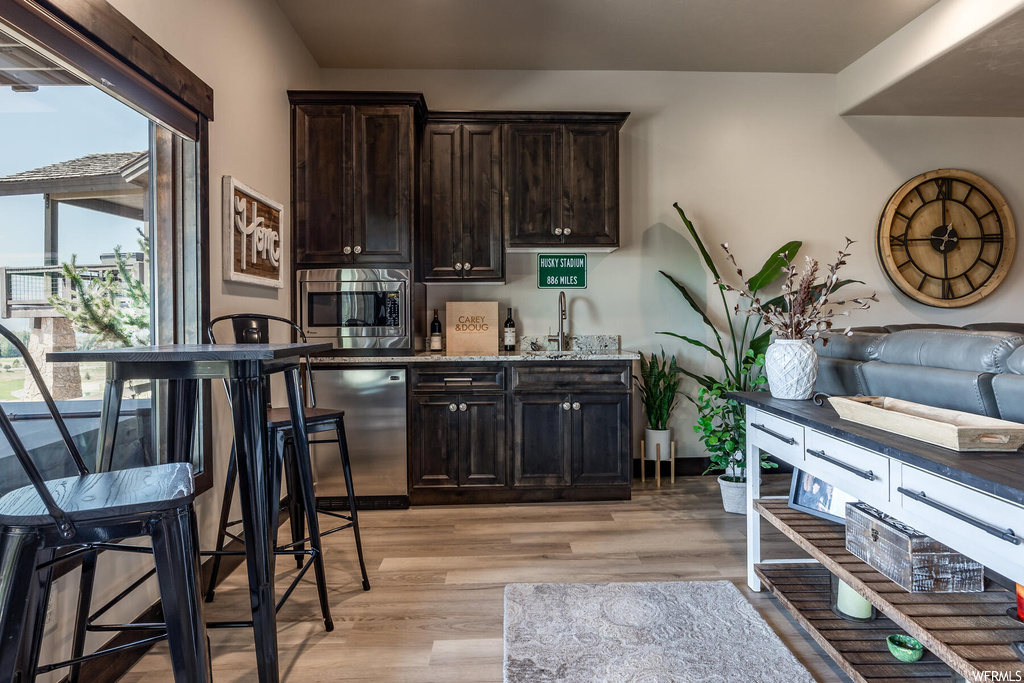 Kitchen featuring dark brown cabinets, stainless steel microwave, light hardwood floors, and dishwashing machine