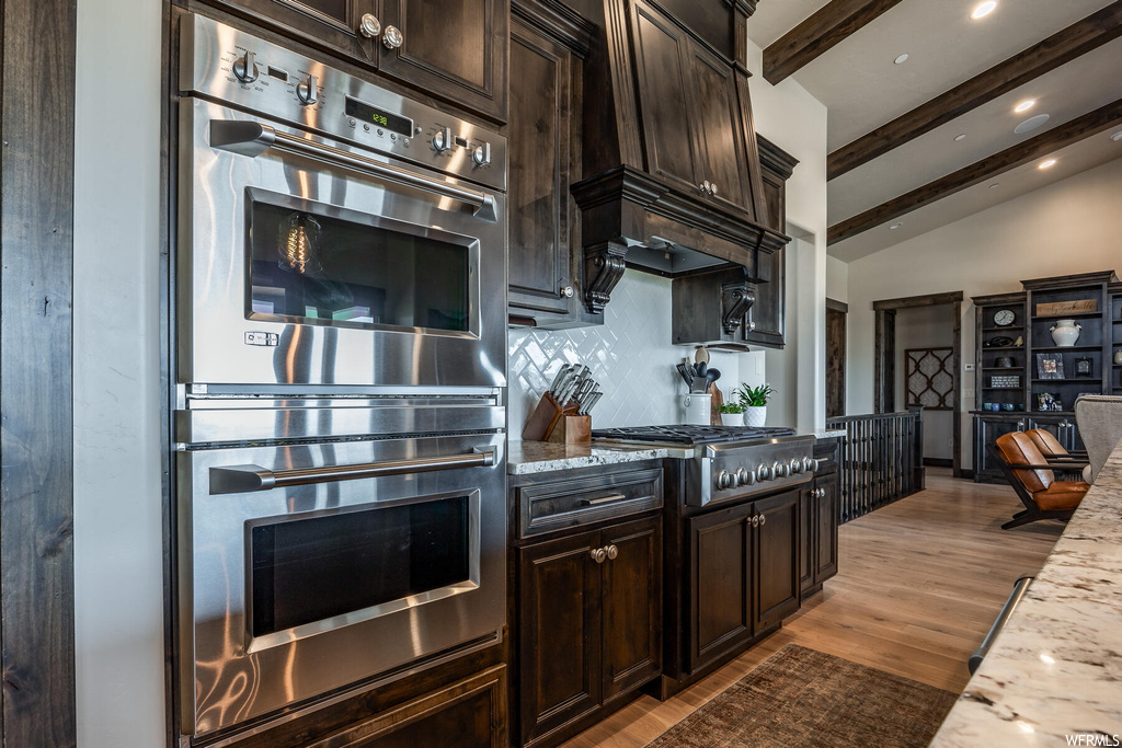 Kitchen with stainless steel appliances, dark brown cabinets, vaulted ceiling with beams, backsplash, and dark parquet floors
