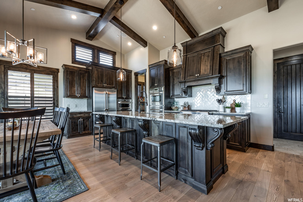Kitchen featuring a high ceiling, dark brown cabinetry, pendant lighting, lofted ceiling with beams, light countertops, stainless steel double oven, backsplash, a kitchen island, and light hardwood floors