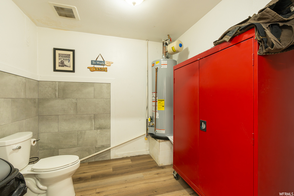 Bathroom featuring gas water heater, light parquet floors, and tile walls