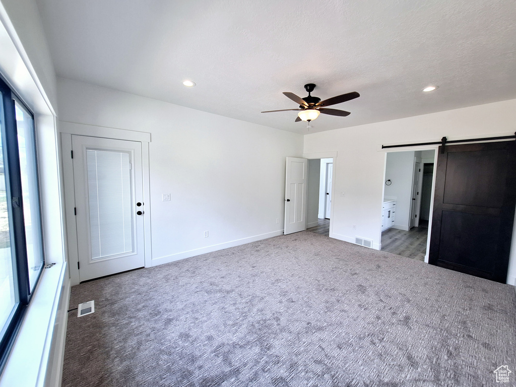 Unfurnished bedroom featuring a barn door, ceiling fan, multiple windows, and light carpet