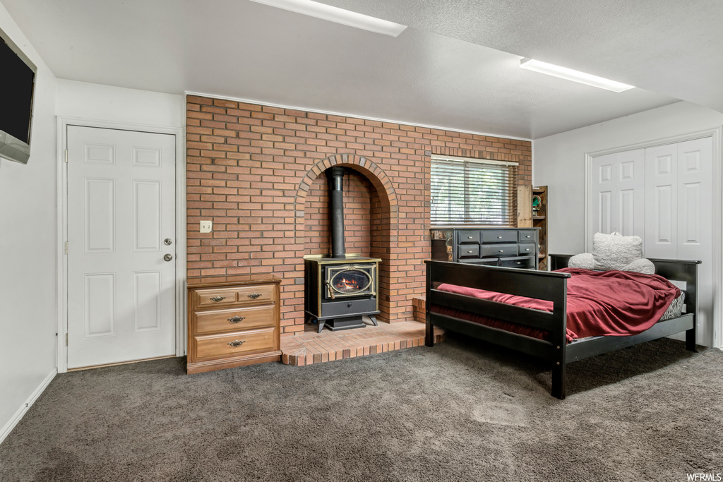 Carpeted bedroom with a fireplace, a textured ceiling, and brick wall