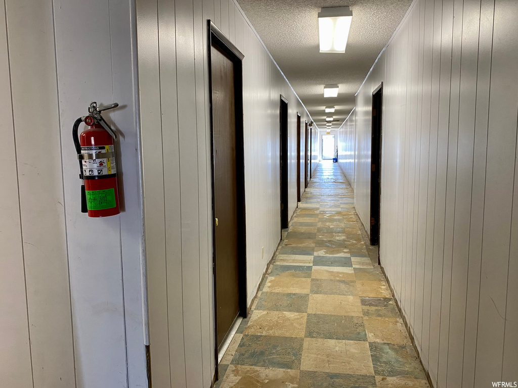 Hall with wood walls, a textured ceiling, and light tile floors