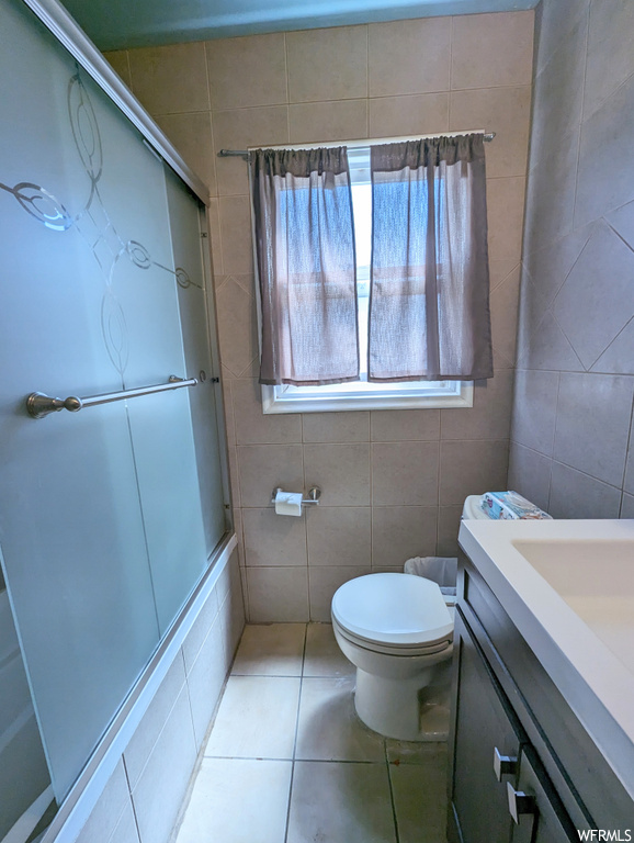Bathroom with light tile floors, tile walls, and vanity