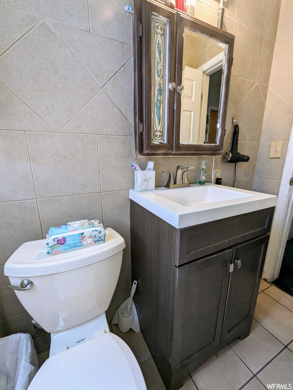Bathroom featuring tile walls, light tile floors, mirror, and vanity with extensive cabinet space