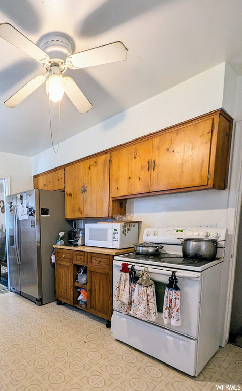 Kitchen with light tile flooring, brown cabinets, white appliances, and ceiling fan