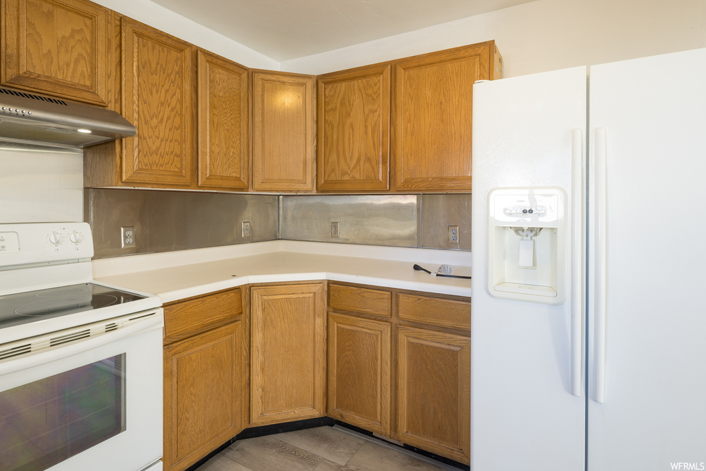 Kitchen with white appliances, backsplash, wall chimney exhaust hood, and light hardwood / wood-style flooring