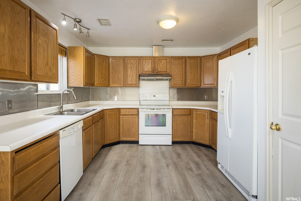 Kitchen featuring sink, rail lighting, white appliances, tasteful backsplash, and light wood-type flooring