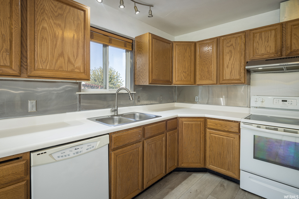 Kitchen with white appliances, backsplash, sink, and light hardwood / wood-style floors