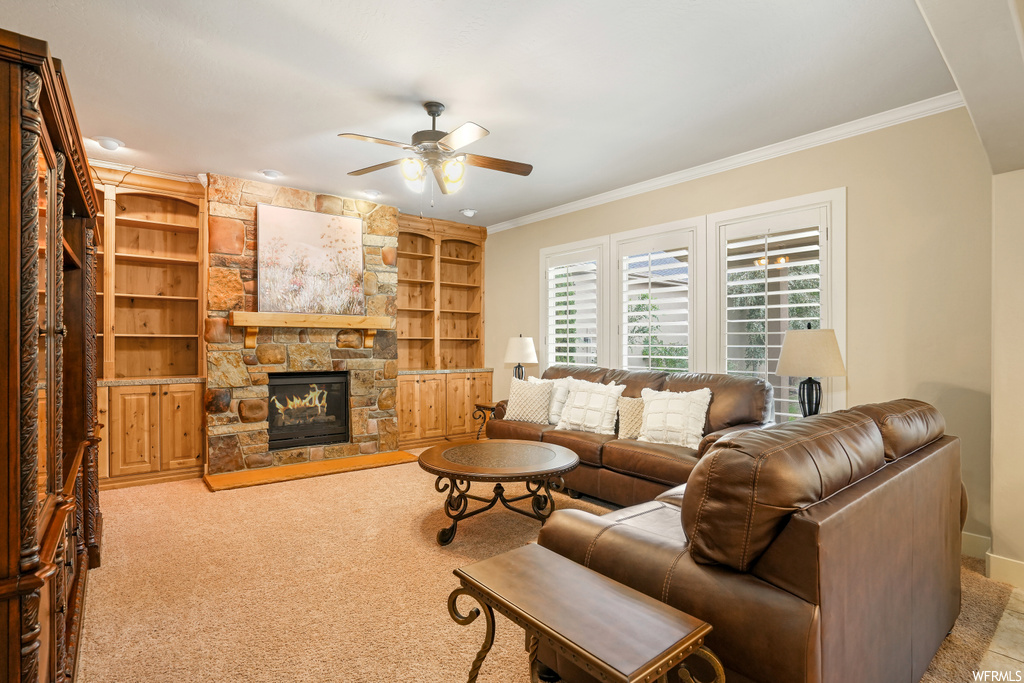 Living room with built in shelves, carpet, crown molding, a fireplace, and ceiling fan