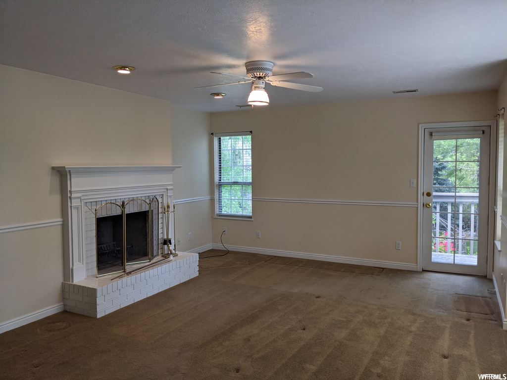 Living room with ceiling fan, dark carpet, a healthy amount of sunlight, and a fireplace