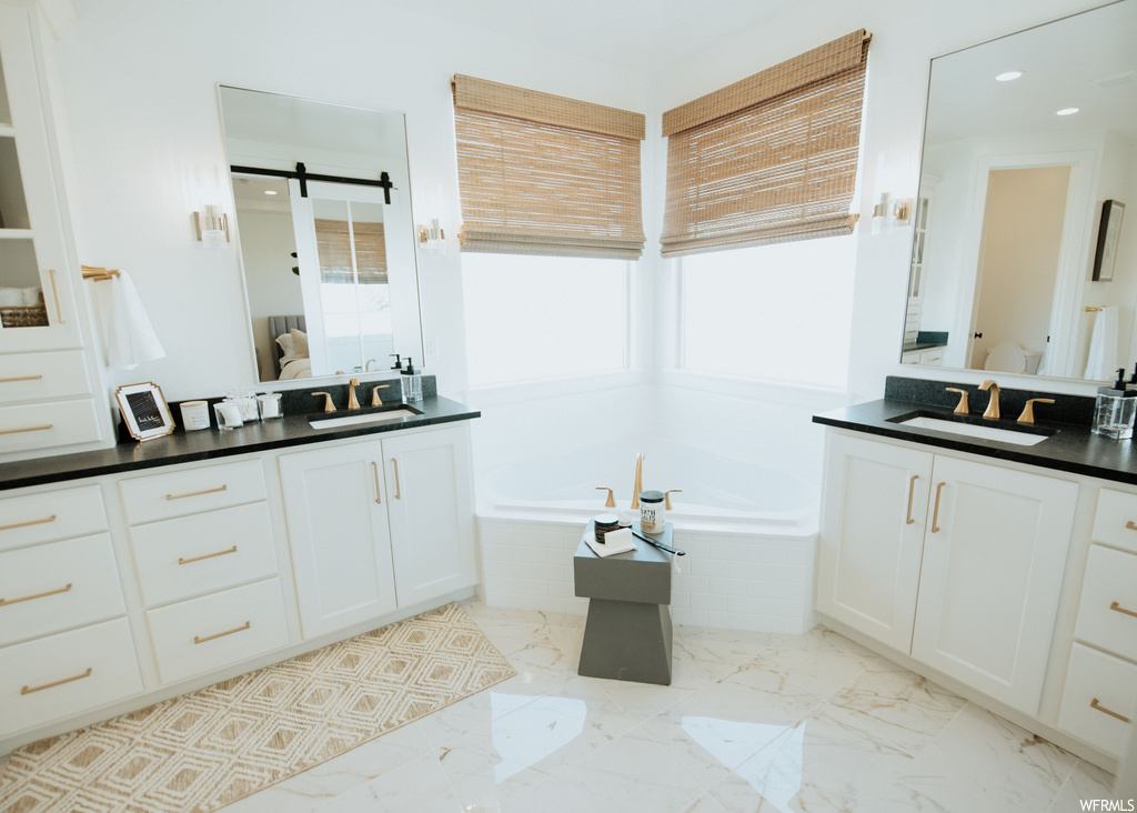 Bathroom featuring light tile floors, mirror, tiled tub, and double vanity