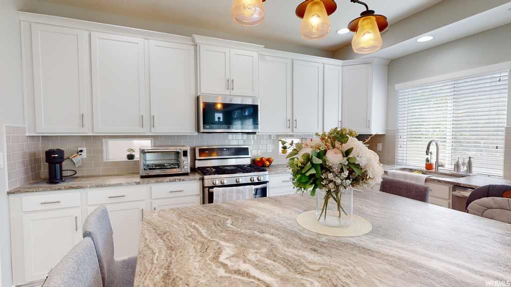 Kitchen featuring white cabinetry, light stone counters, appliances with stainless steel finishes, and backsplash