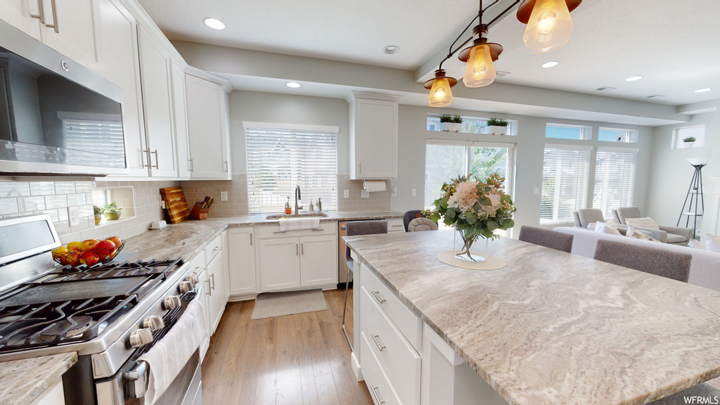Kitchen featuring light parquet floors, stainless steel appliances, pendant lighting, light countertops, white cabinets, and backsplash