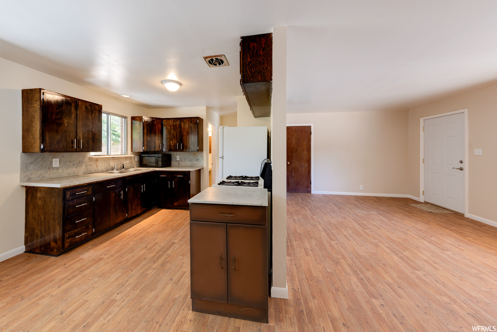 Kitchen featuring white refrigerator, dark brown cabinets, backsplash, an island with sink, light countertops, and light hardwood flooring