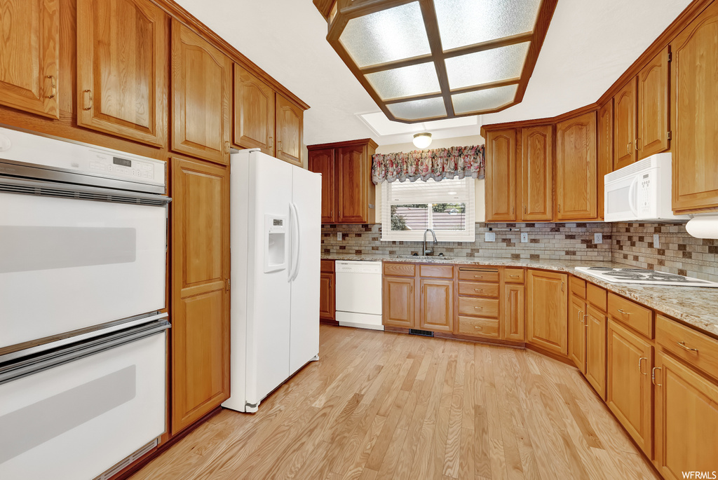 Kitchen with white appliances, brown cabinets, light countertops, backsplash, and light hardwood floors