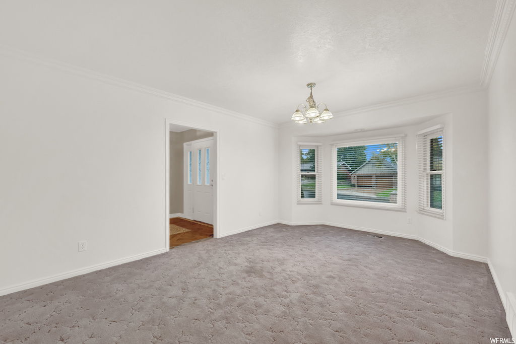 Carpeted empty room featuring an inviting chandelier and ornamental molding