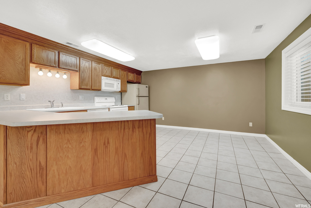Kitchen featuring light tile floors, brown cabinets, white appliances, and light countertops